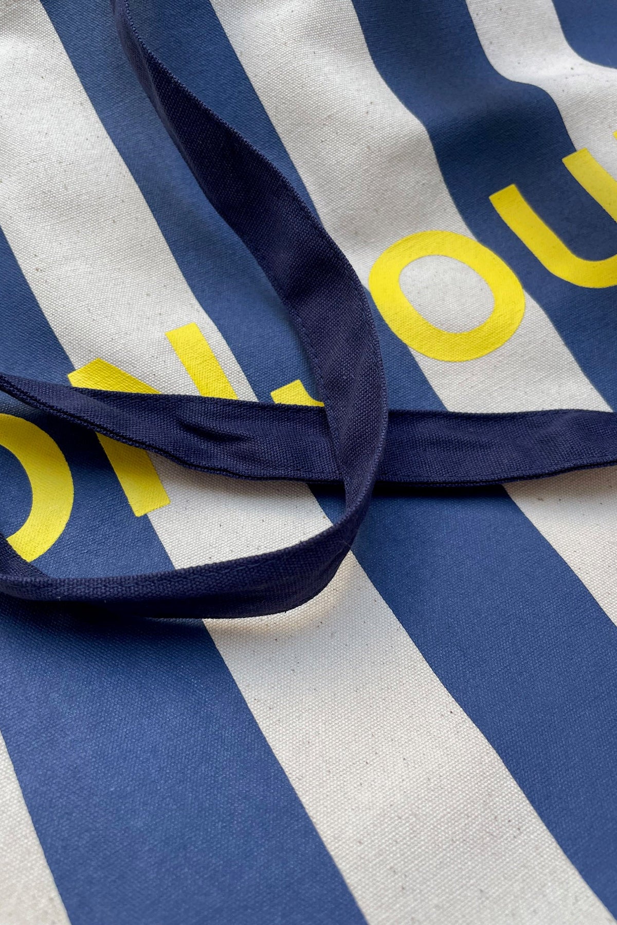 Close-up of a striped fabric item with navy blue and off-white vertical stripes, featuring yellow printed lettering and dark navy straps.
