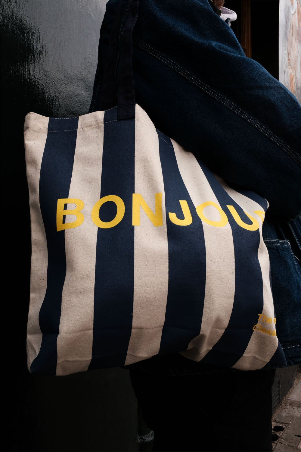 Striped tote bag with 'BONJOUR' text held by a person