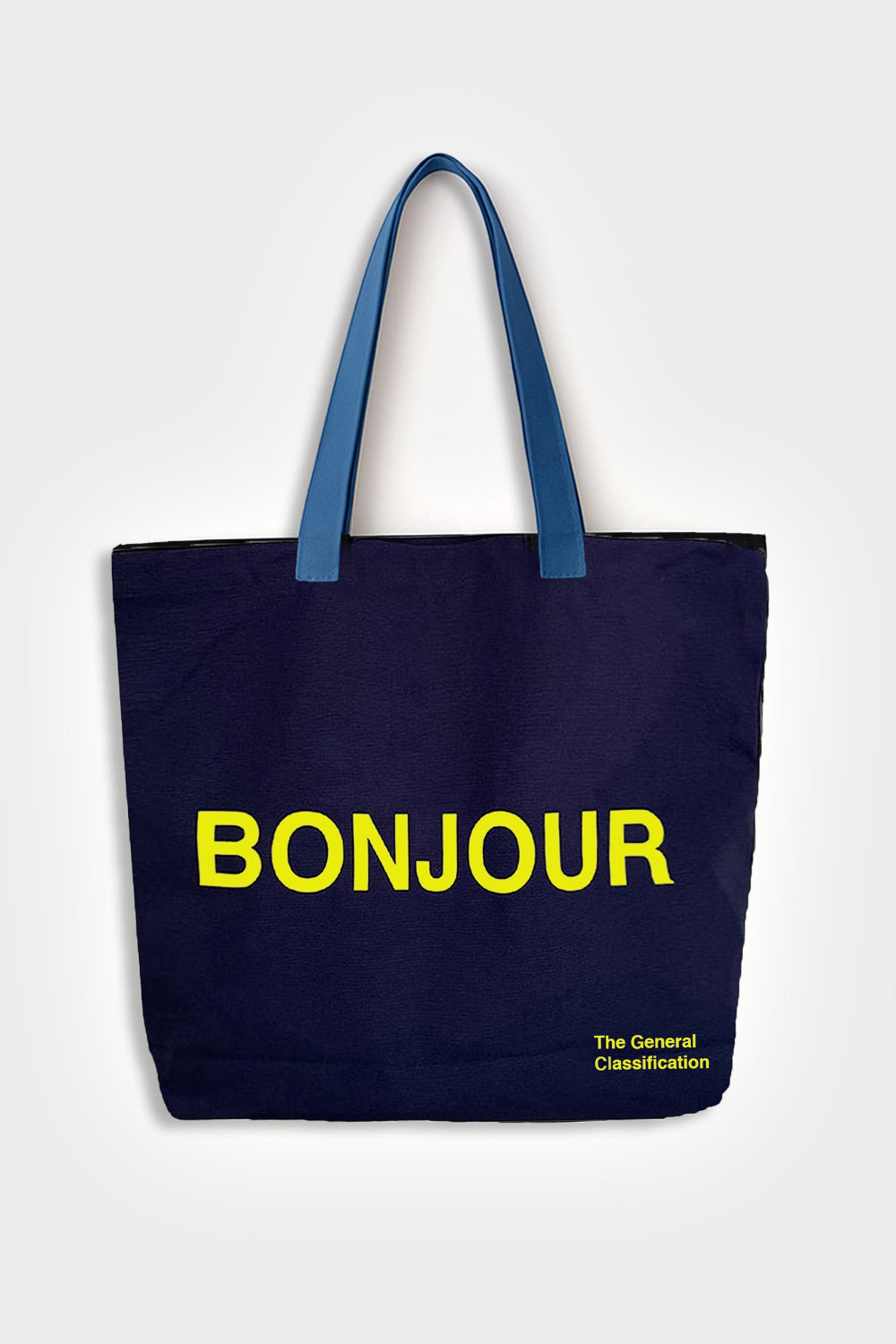 A navy blue canvas tote bag with blue handles and bold yellow text reading 'BONJOUR' on the front, with smaller yellow text 'The General Classification' in the bottom right corner, shown against a light grey background.
