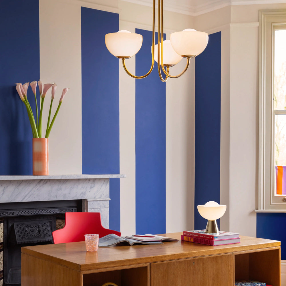 Modern living room with blue striped wall, wooden desk, and red chair.