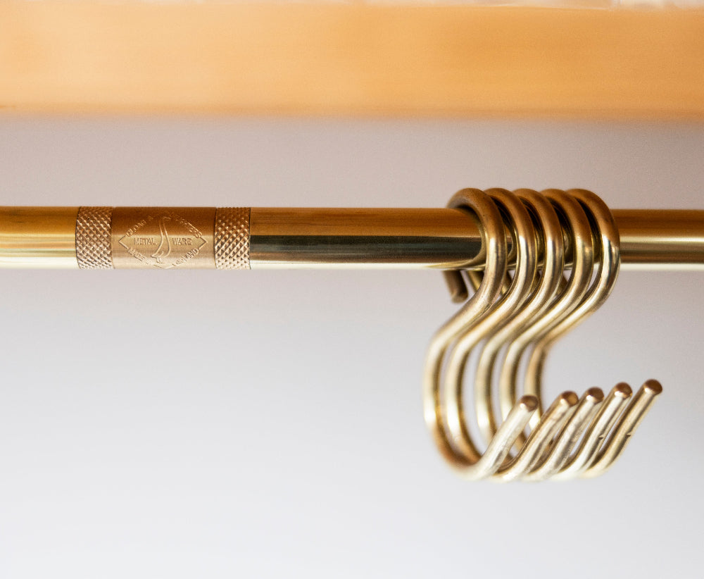 Close-up of a brass kitchen rod with a knurled decorative band and a set of matching S-hooks hanging from the rod.