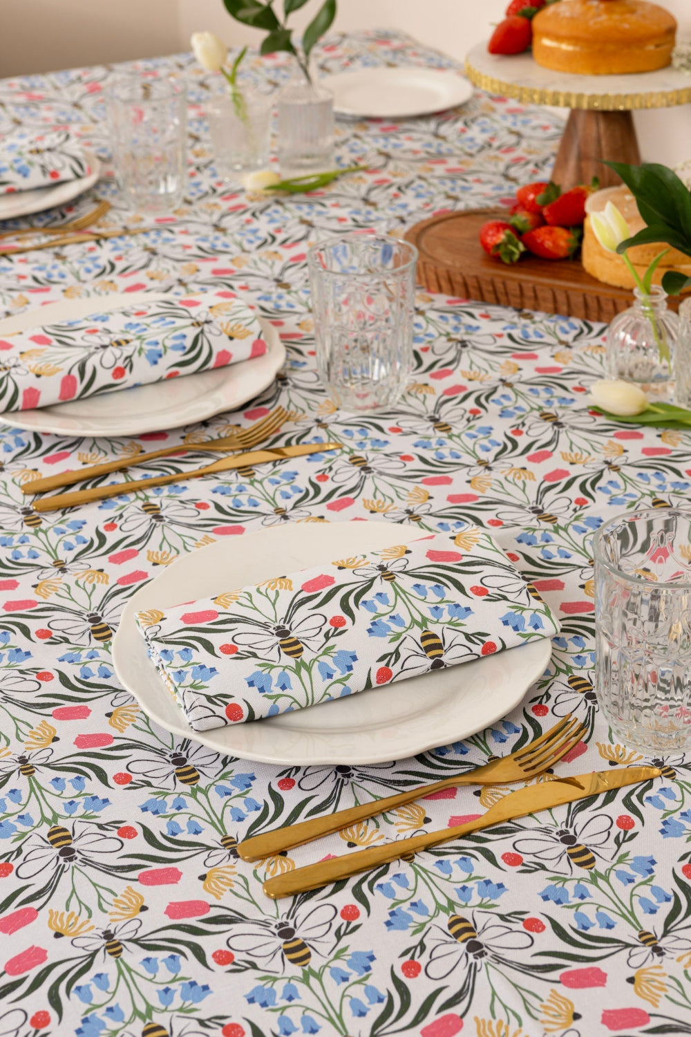 Dining table set with floral tablecloth, plates, cutlery, and fruits.