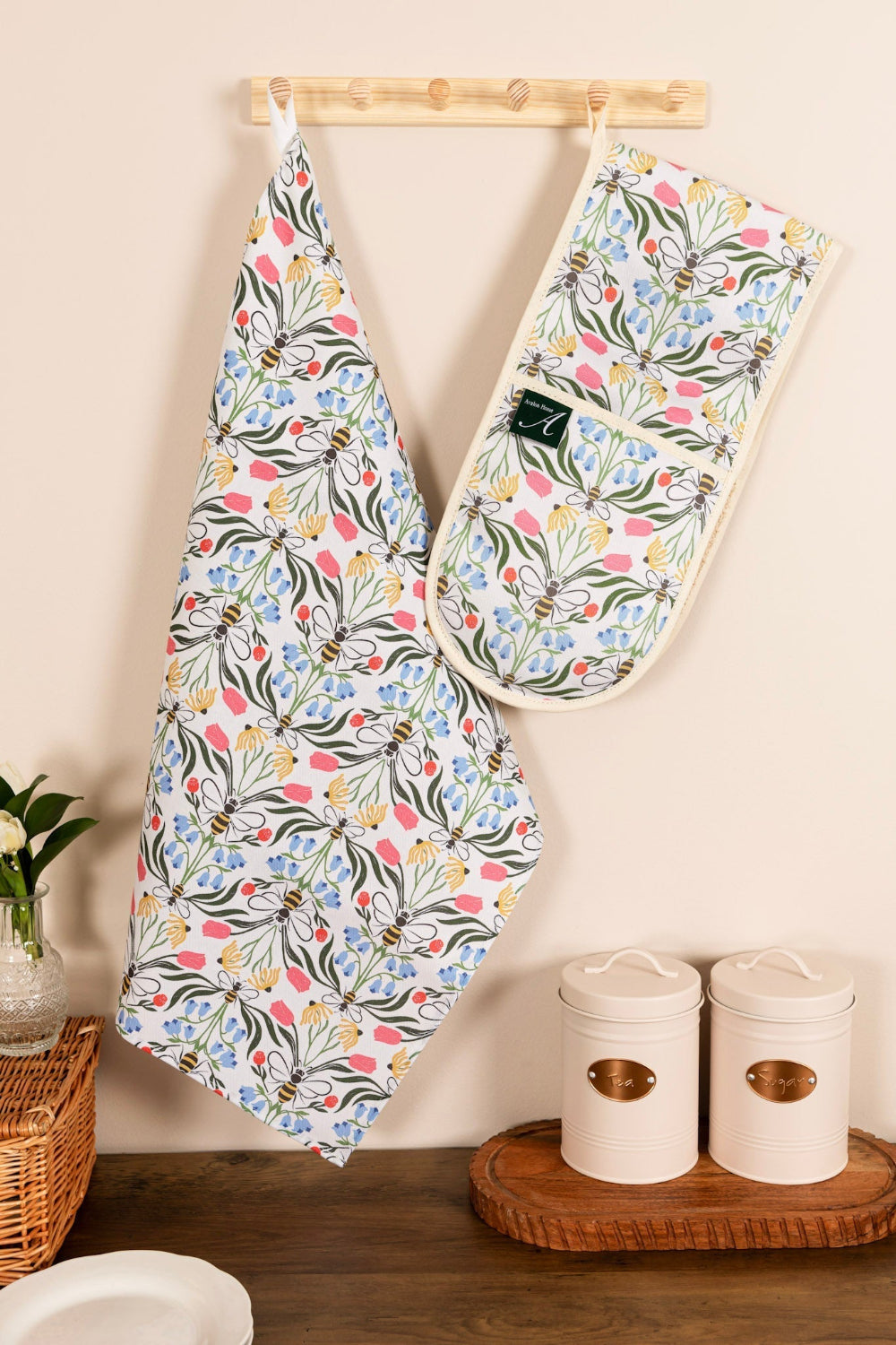 Floral-patterned tea towel and oven mitt hanging on a wooden rack against a beige wall.