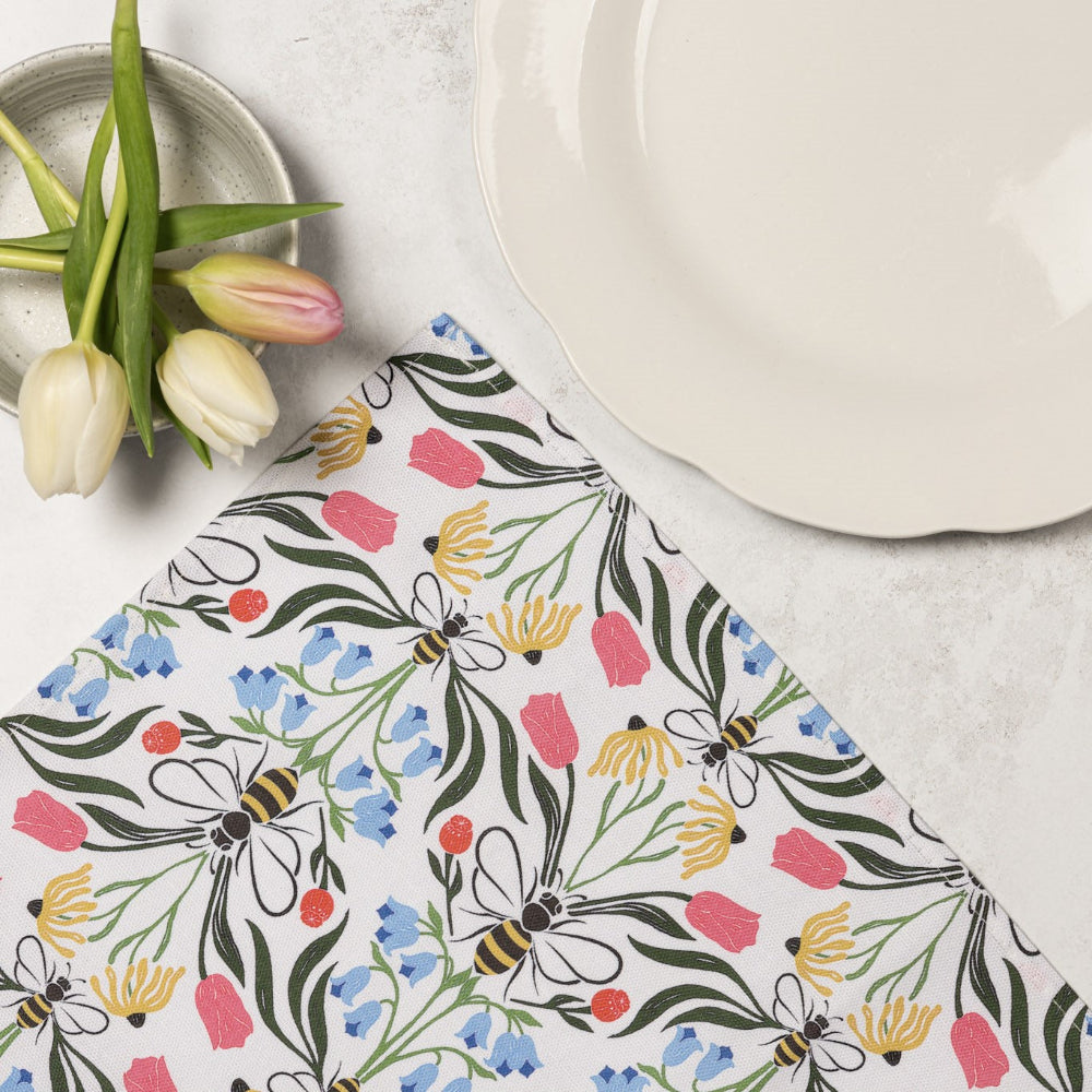 Floral and bee-patterned napkin on a table with tulips and plates.