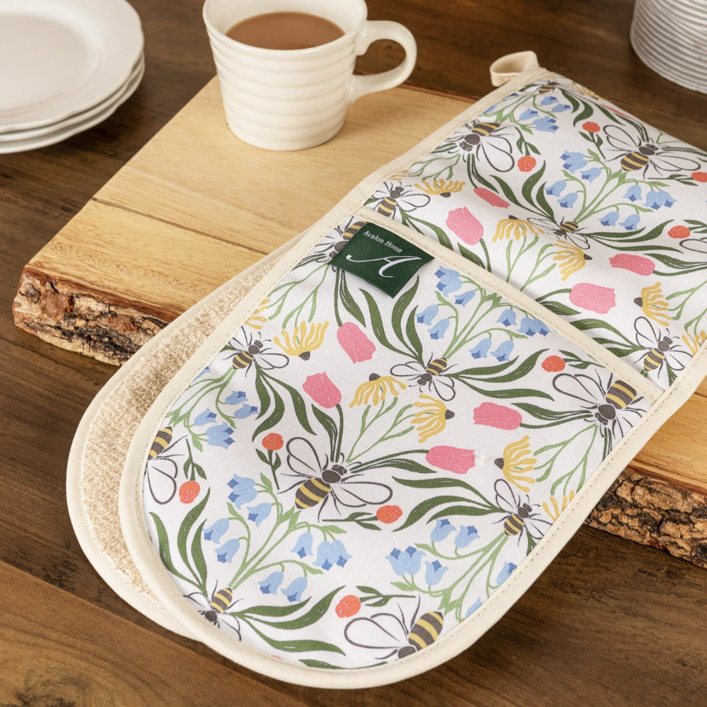 Floral and bee-patterned oven mitt on a wooden surface with a cup of coffee.