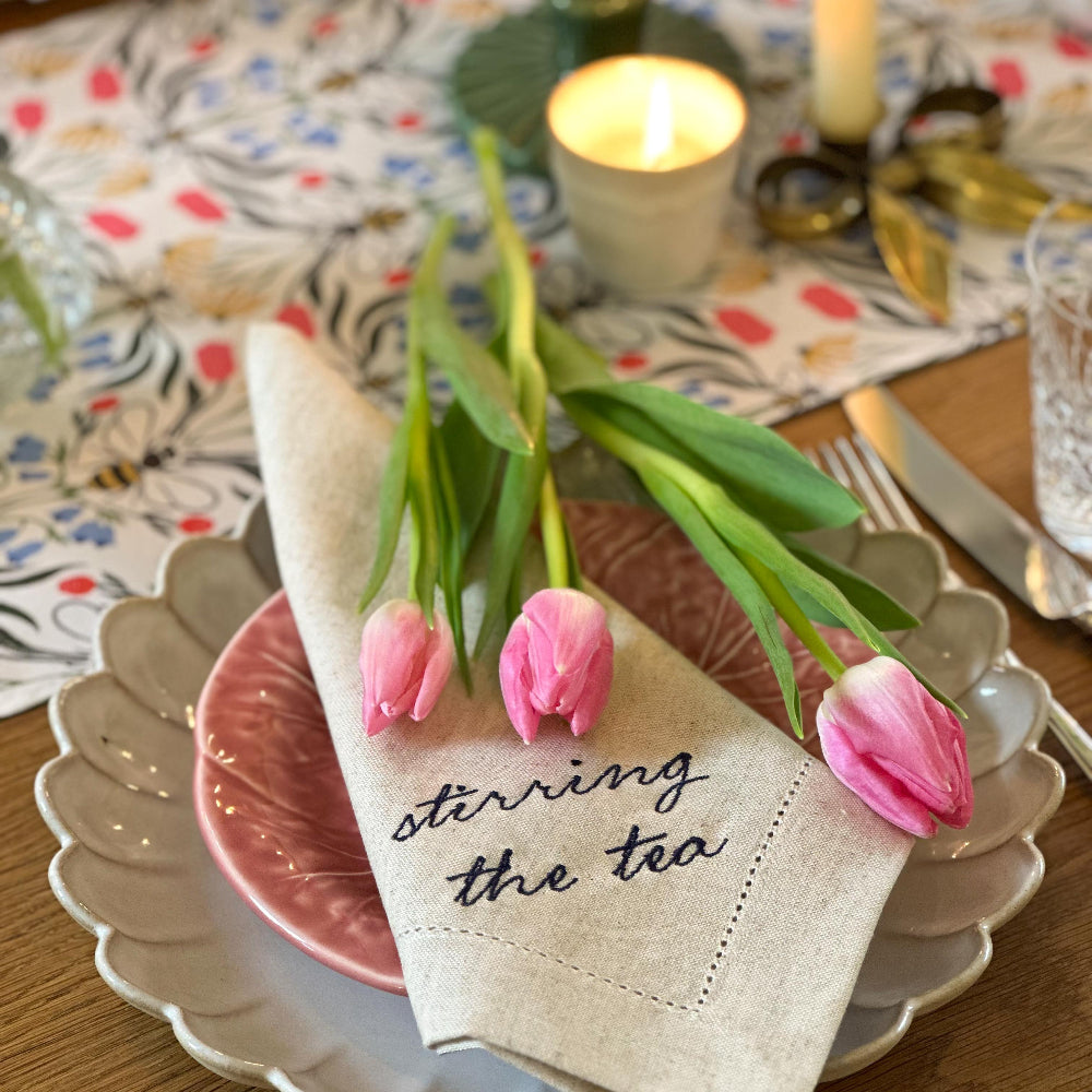 Napkin with tulips and text 'stirring the tea' on a table setting with plates and candles.