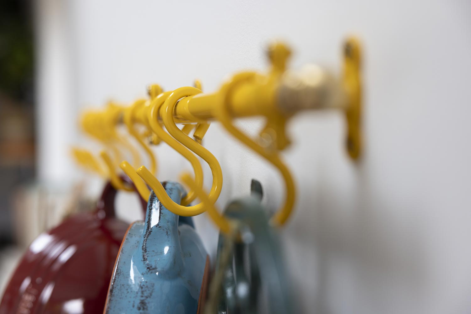 A close-up of a yellow metal kitchen rack with multiple curved hooks, shown holding colourful ceramic mugs against a plain light background.
