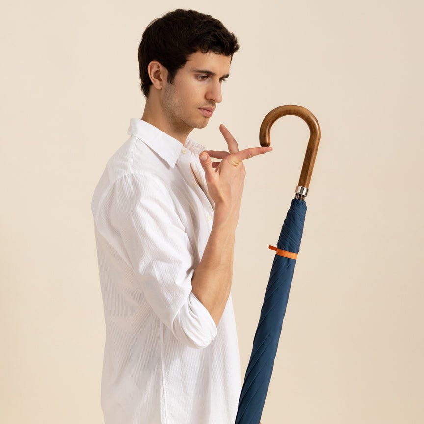 Man holding a blue umbrella with a wooden handle against a beige background