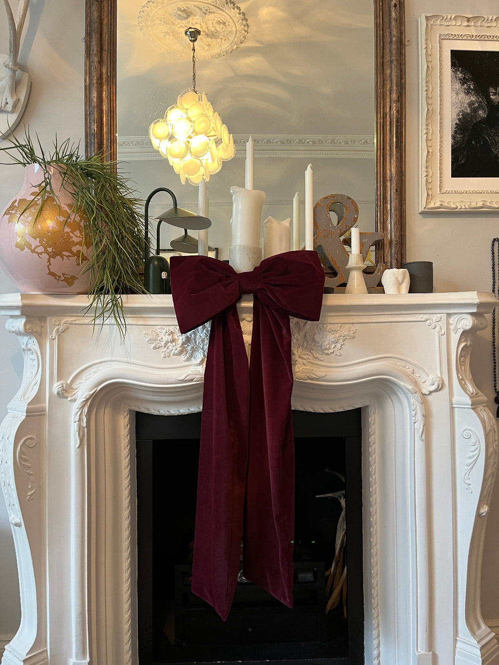 Burgundy velvet Christmas bow styled above a fireplace mantel