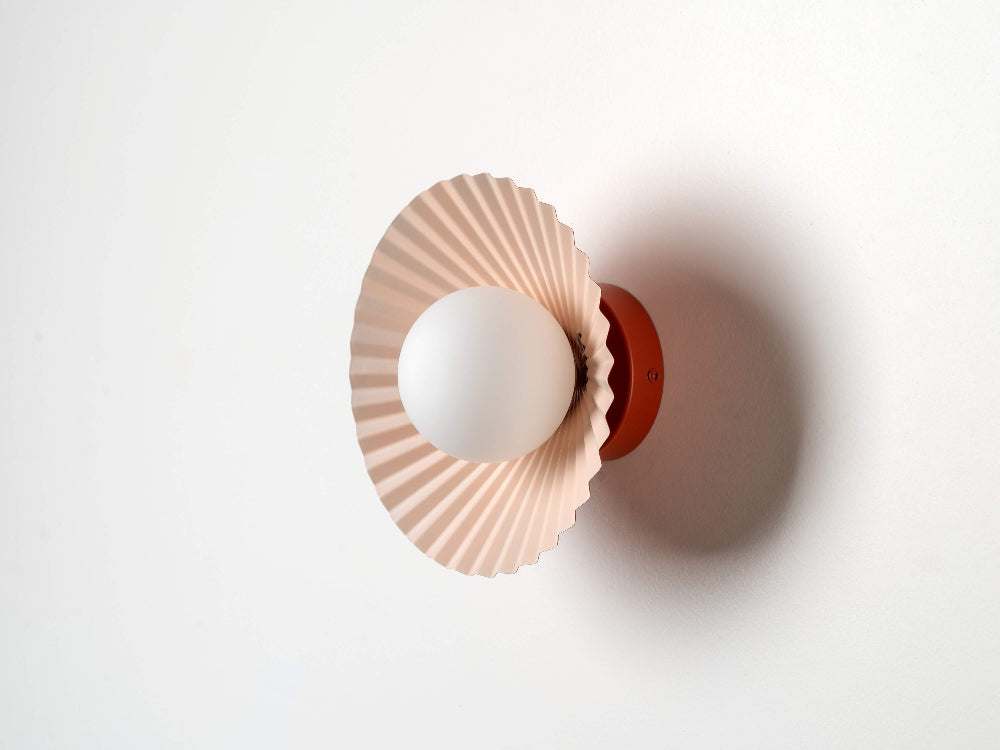Illuminated pleated wall light with a soft pink interior and glowing glass shade