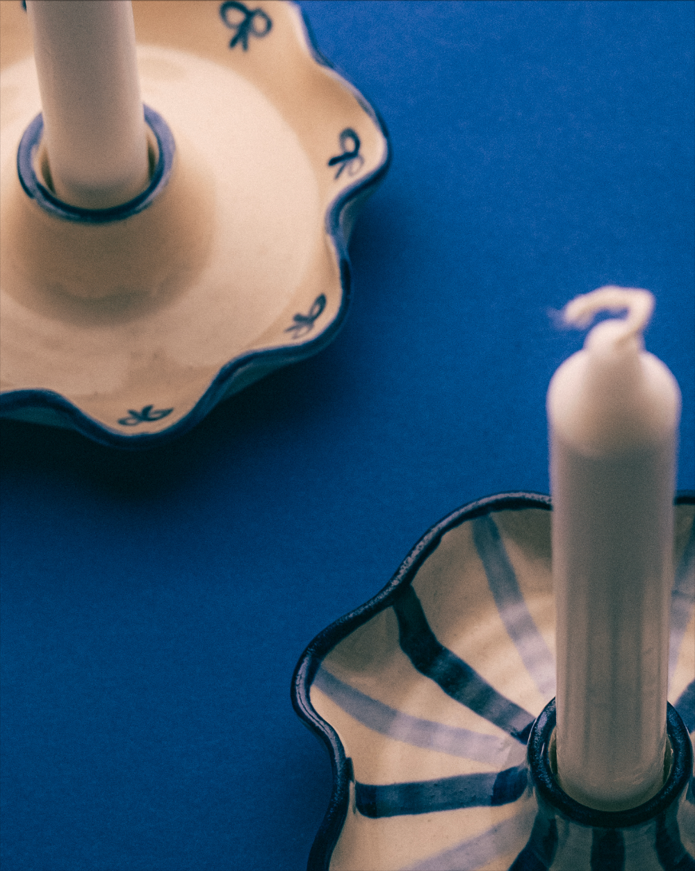 Two white candles in decorative holders on a blue surface