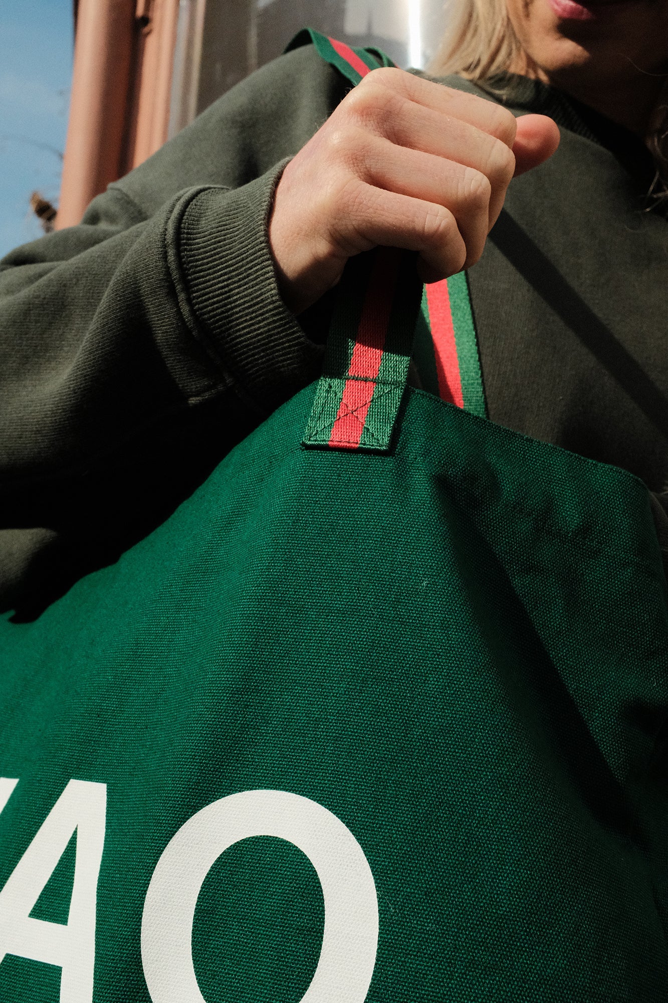 Person holding a green bag with a brand logo, wearing a dark green jacket.