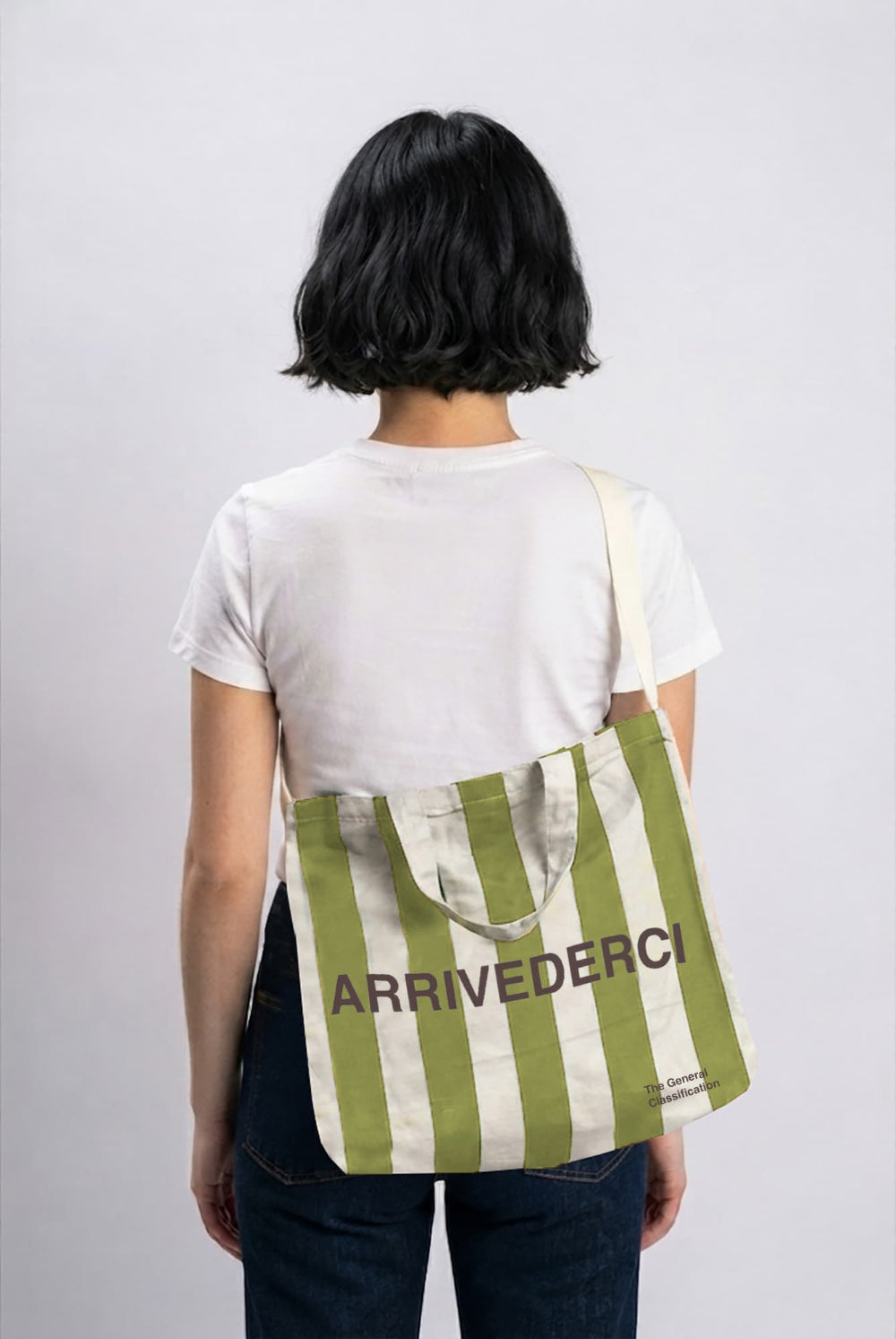 A person shown from behind wearing a white t-shirt and dark jeans, carrying a green and white striped canvas tote bag with the brand name 'ARRIVEDERCI' printed on the front.