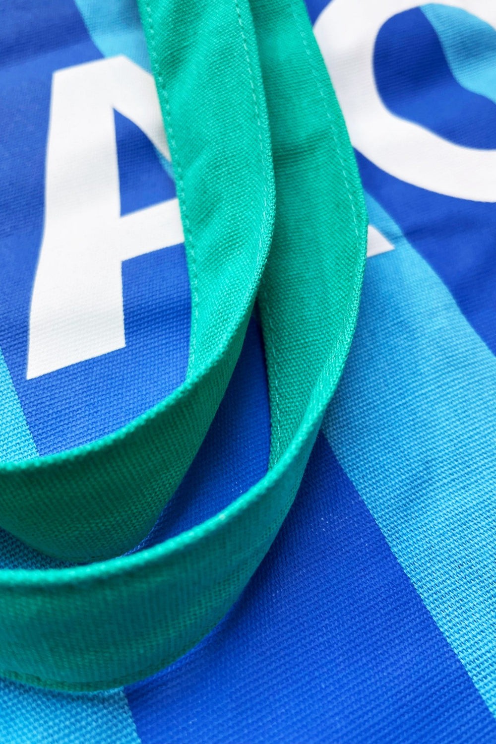 Close-up of a blue and light blue striped fabric item with a bright green woven strap and white lettering.