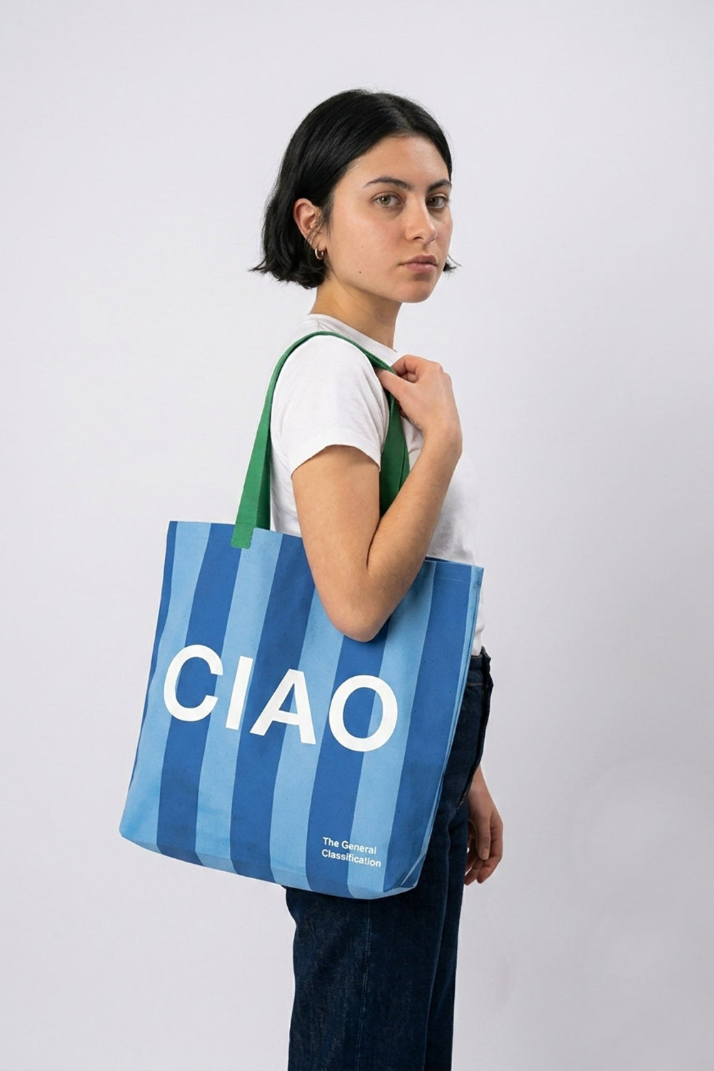 Person holding a blue and green striped tote bag with 'CIAO' printed on it against a white background
