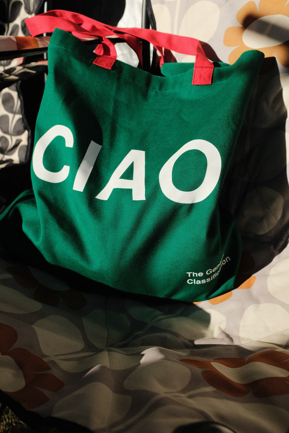 Green tote bag with 'CIAO' printed on it, placed on a reflective surface.