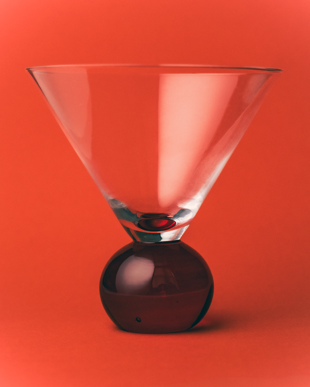 Clear glass martini glass with a dark base on a red background