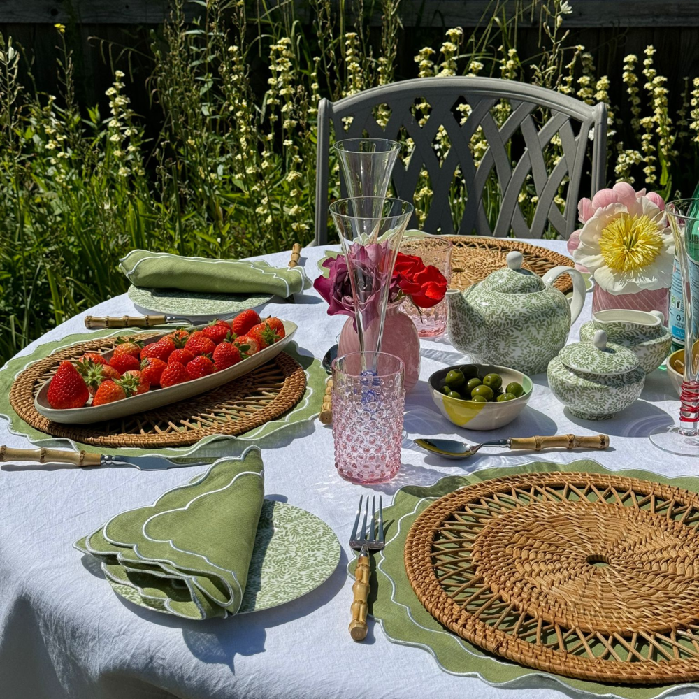 Outdoor table setting with strawberries, teapot, and flowers in a garden.