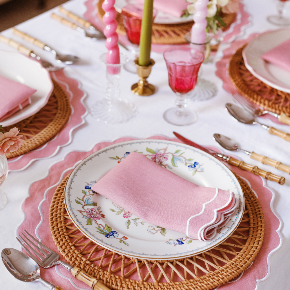 Elegant table setting with pink scalloped napkins, glasses, and cutlery on a white tablecloth.