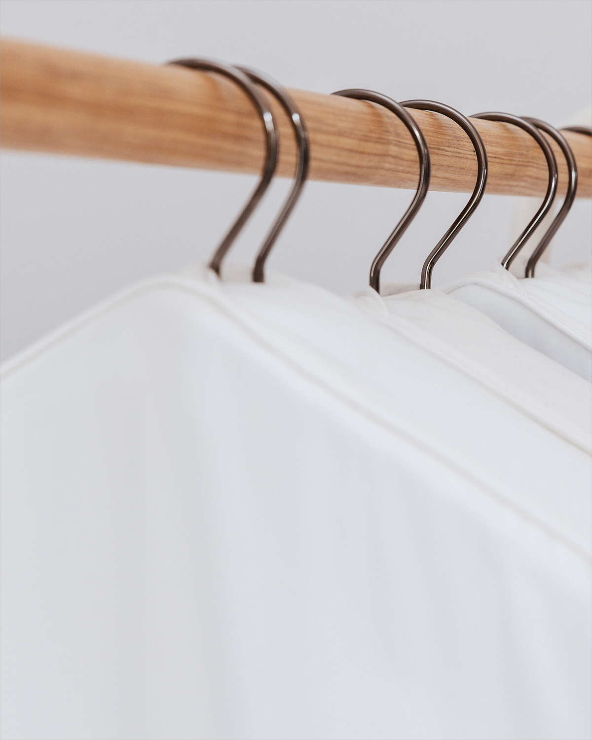 White organic cotton clothes cover on a wooden hanger with metal hooks against a light background