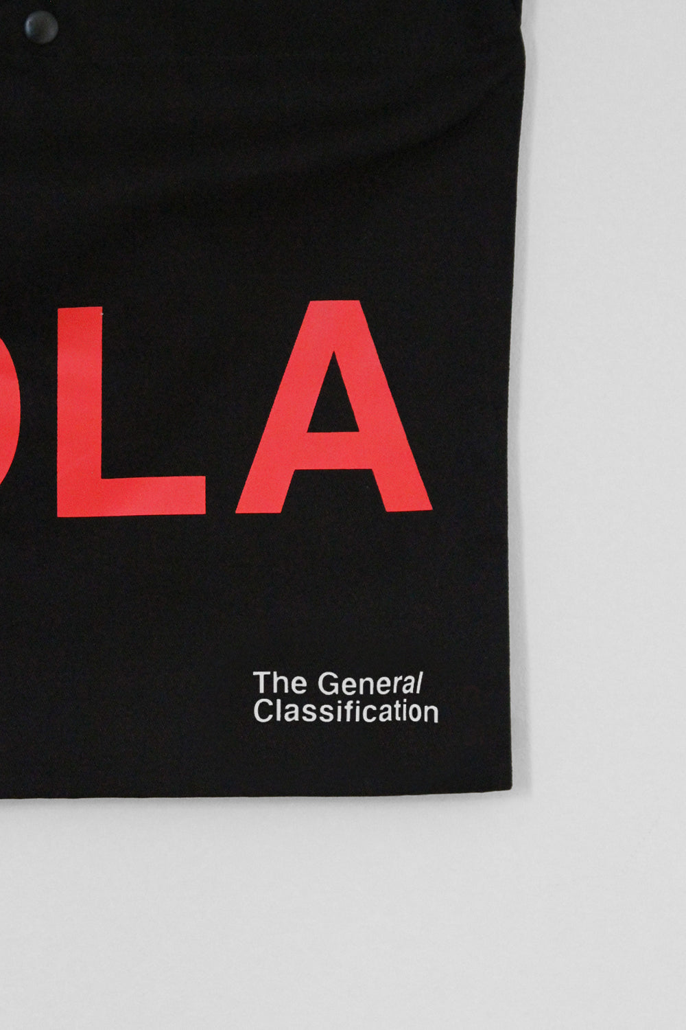Close-up of a black garment with large red letters and white text reading 'The General Classification' on a light grey background.