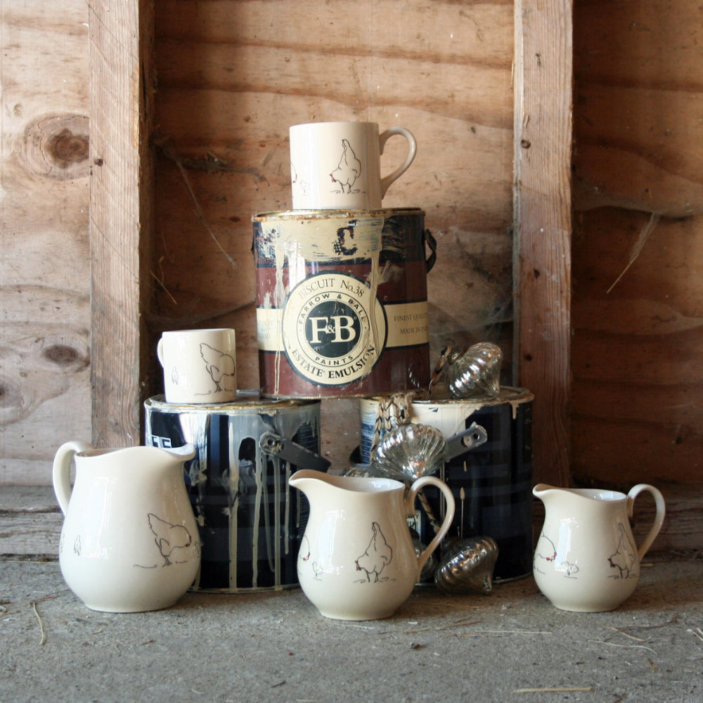 Collection of ceramic pitchers and a paint tin can on a wooden shelf.