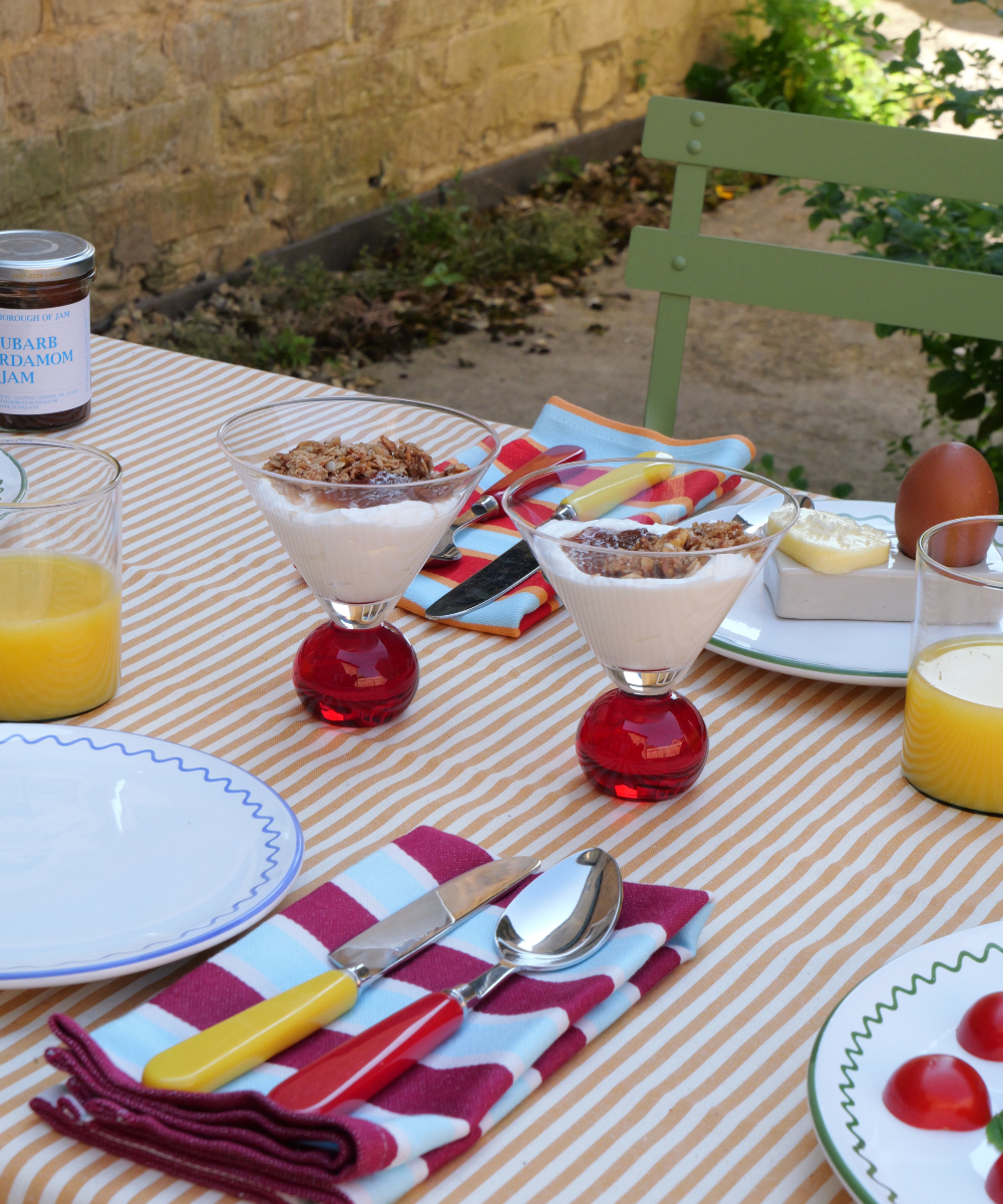 Outdoor table setting with breakfast items including yogurt, fruit, and orange juice.