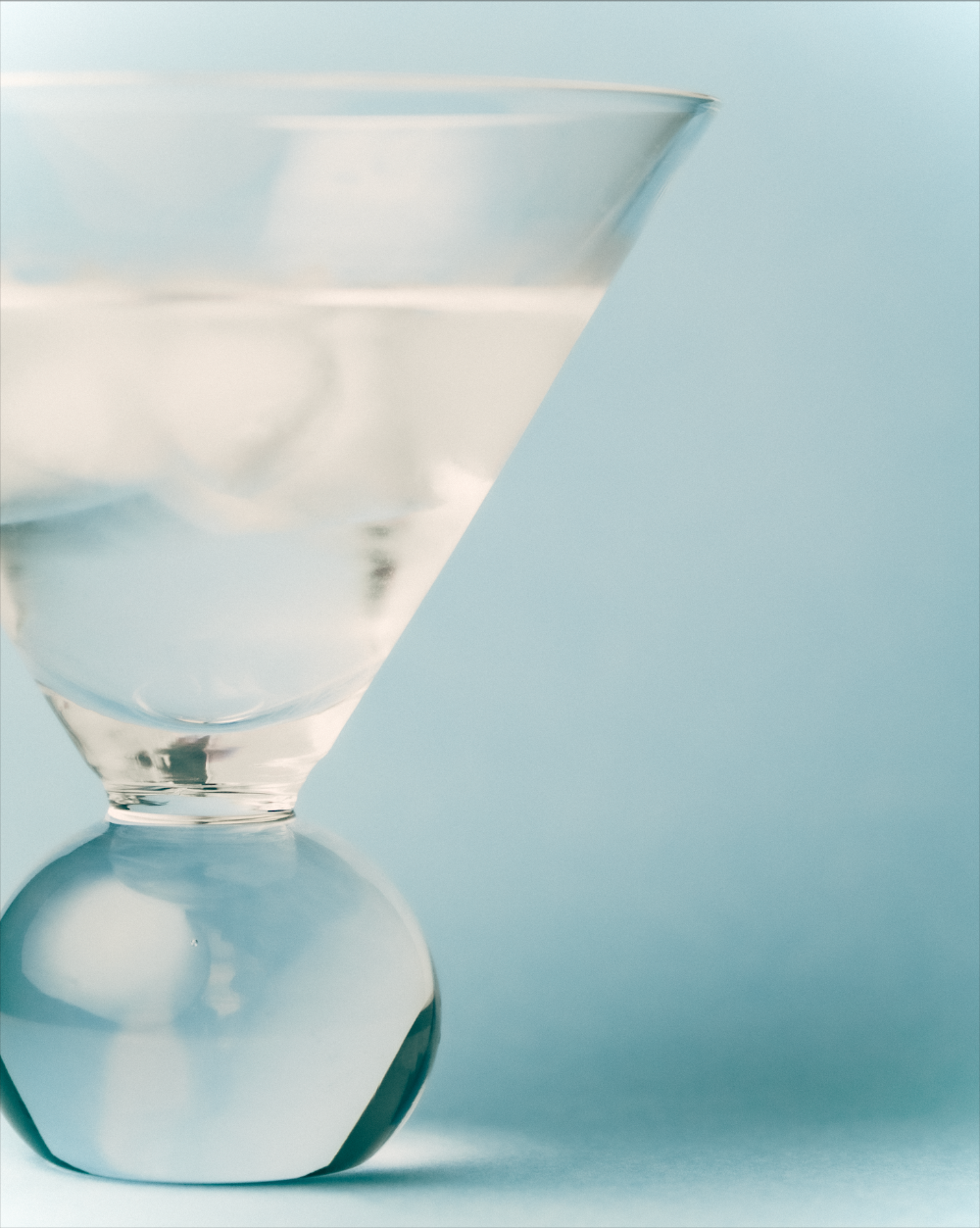 Clear glass cocktail glasses with bobble stems on a light blue background