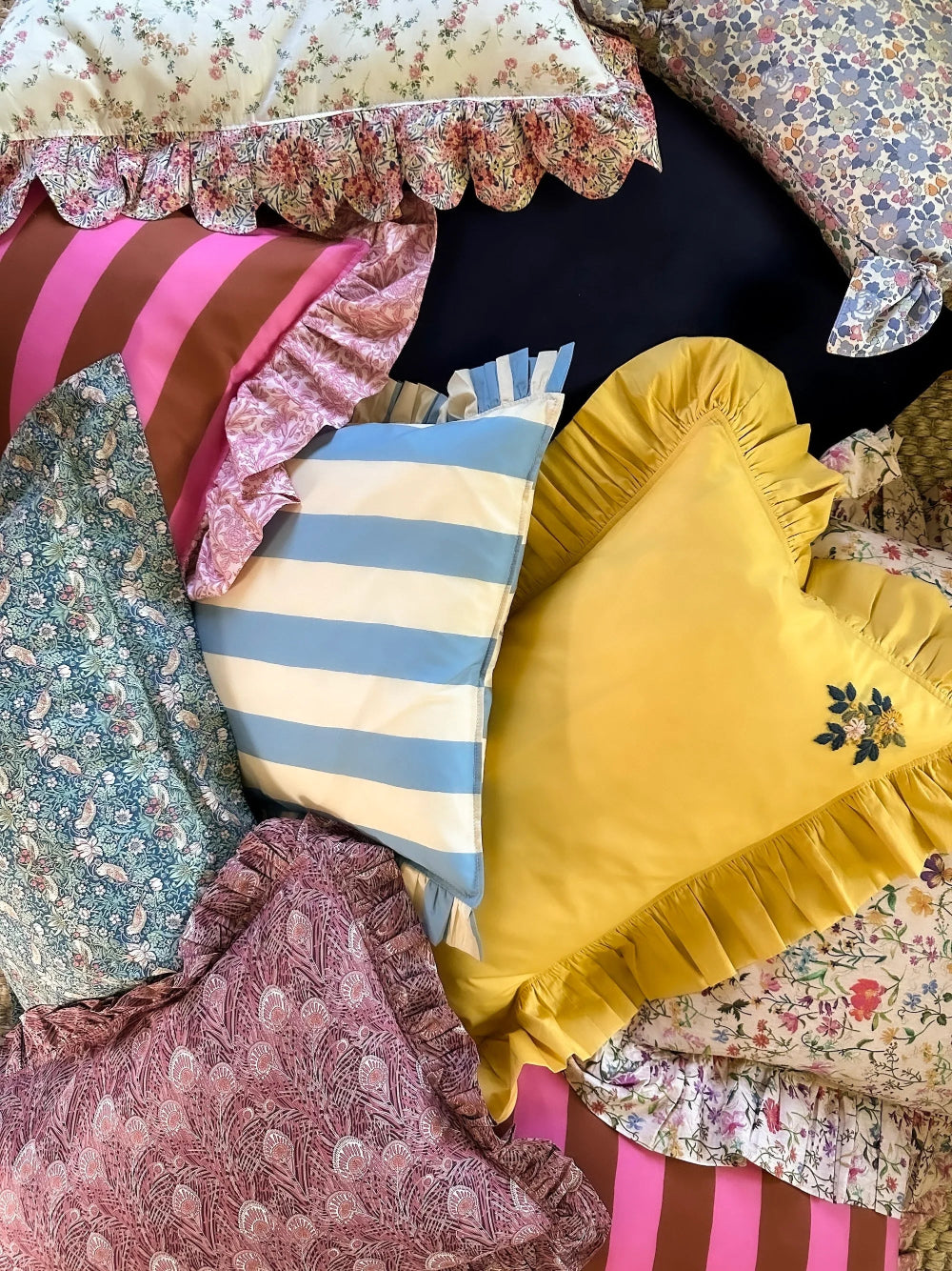 Assorted colourful pillows with floral, striped, and solid patterns on a dark surface.
