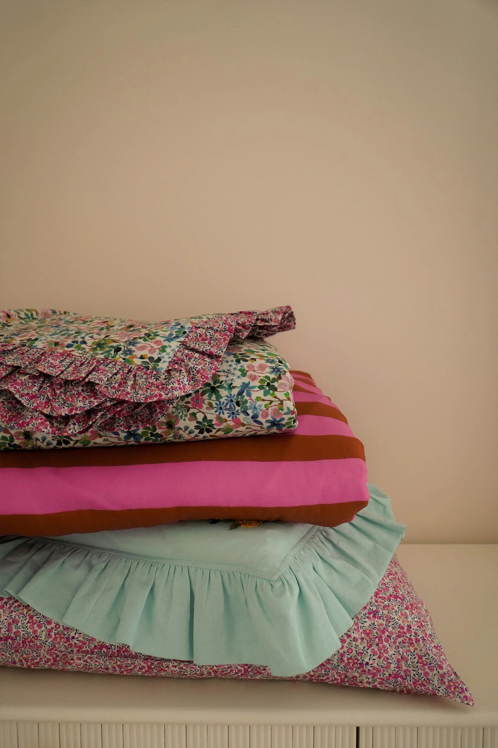 Stack of colourful ruffled cushions on a beige surface with a beige background