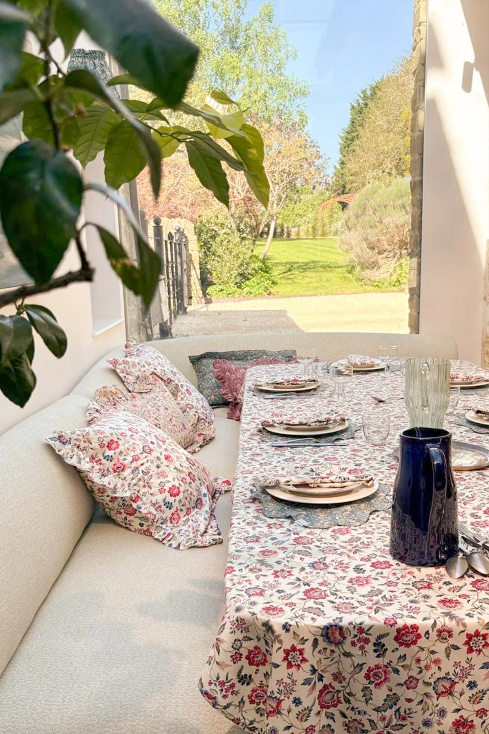 Outdoor seating area with floral tablecloth and cushions, overlooking a garden.