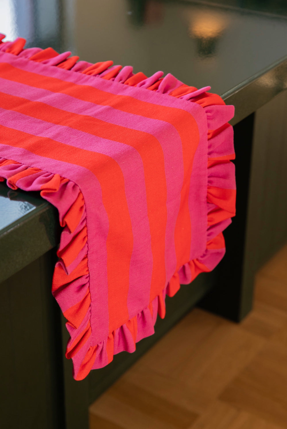 A bright pink and orange striped table runner with ruffled edges draped over a dark table on a wooden floor.