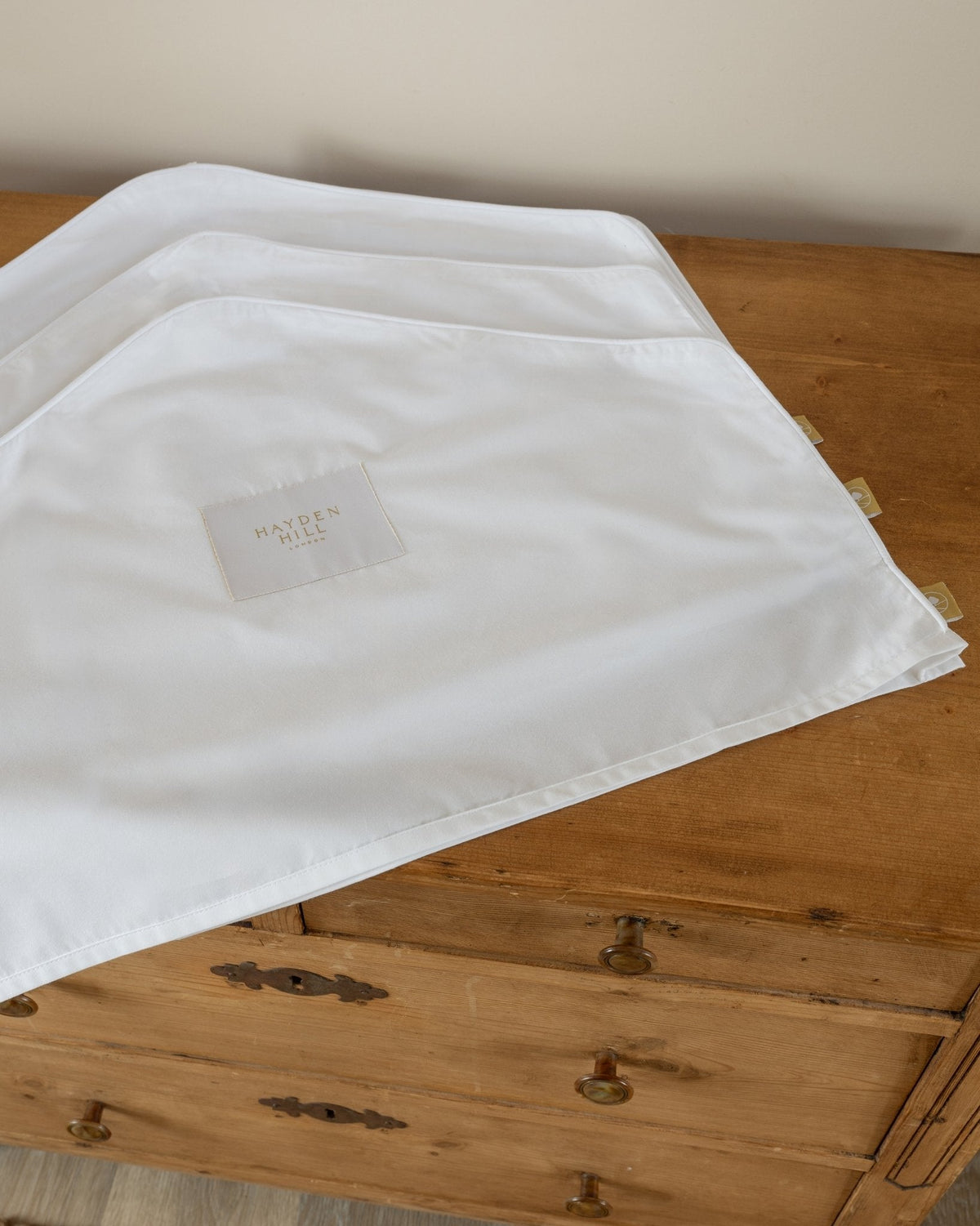White organic dust covers for jackets and jumpers with Hayden Hill logo on a wooden surface