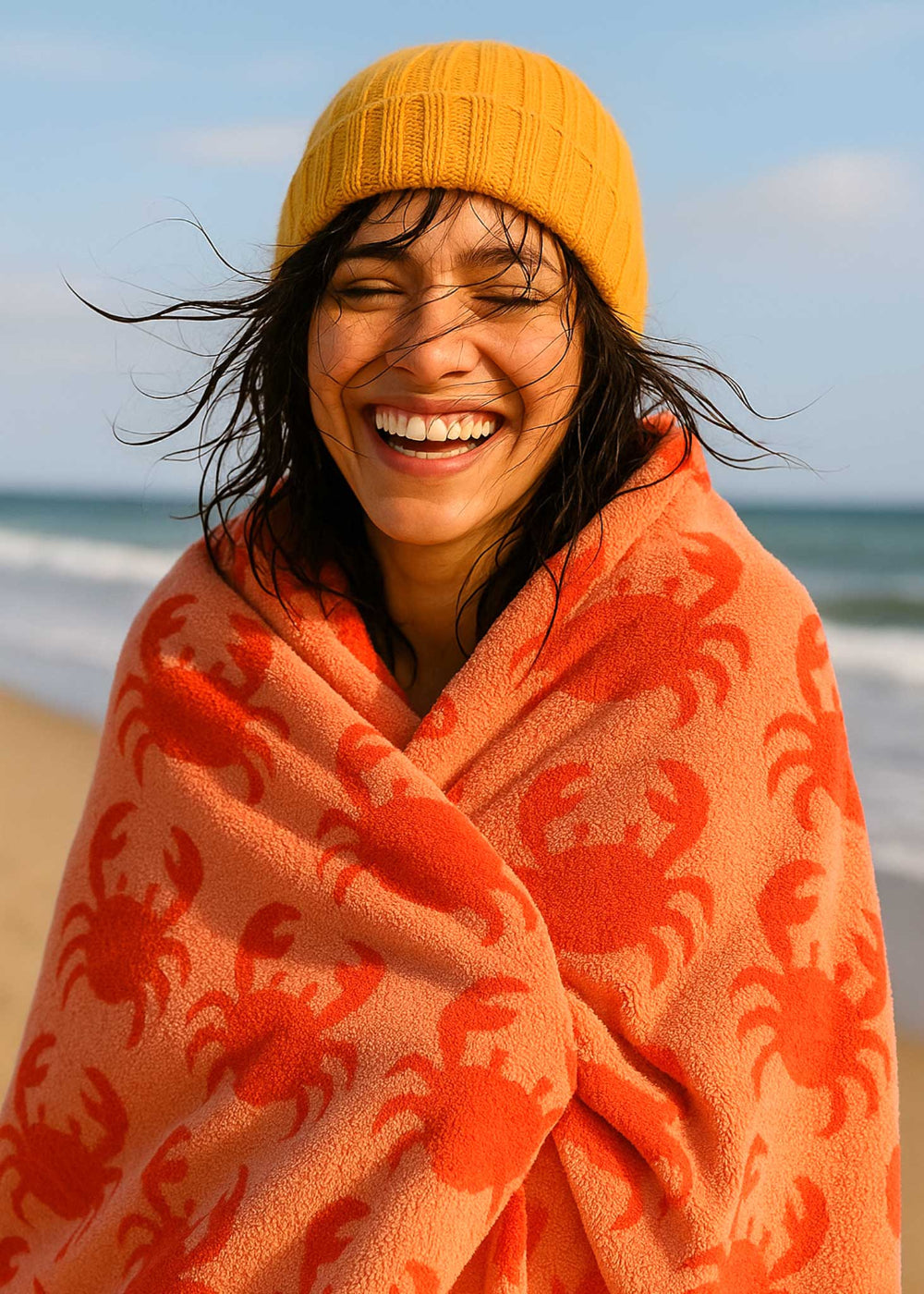 Person wrapped in a red crab-patterned blanket on a beach