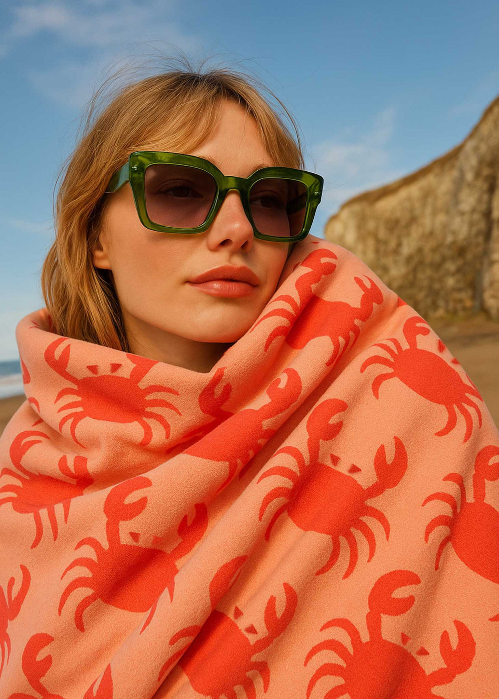 Woman wearing a pink scarf with red crab patterns on a beach.