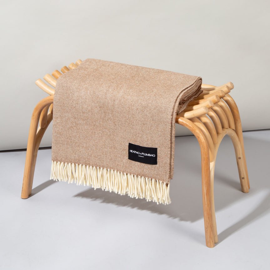 Beige blanket with a brand label draped over a wooden stool on a light grey background