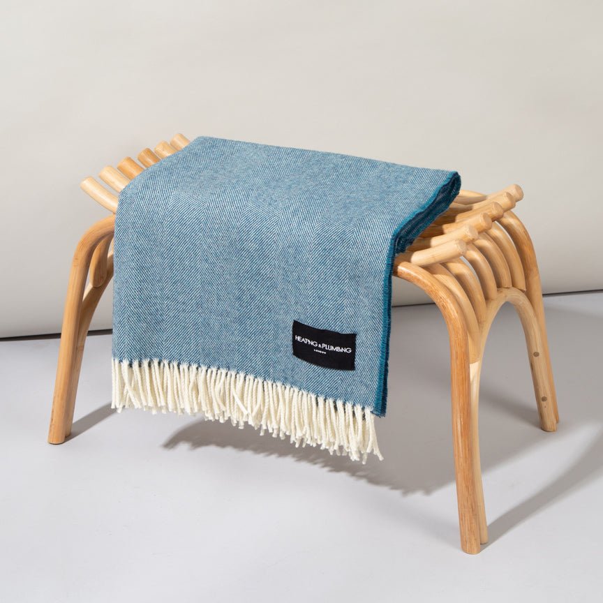 Blue blanket with white fringe draped over a wooden stool on a light grey background