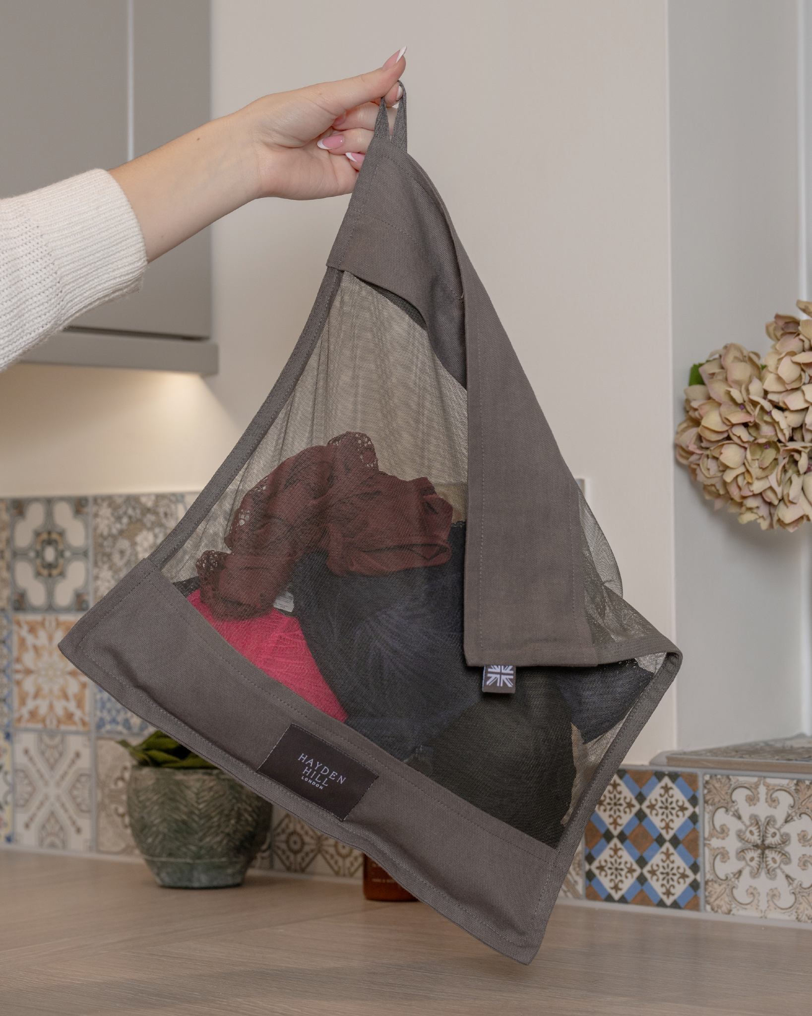 Person holding a gray mesh bag with shoes against a kitchen background
