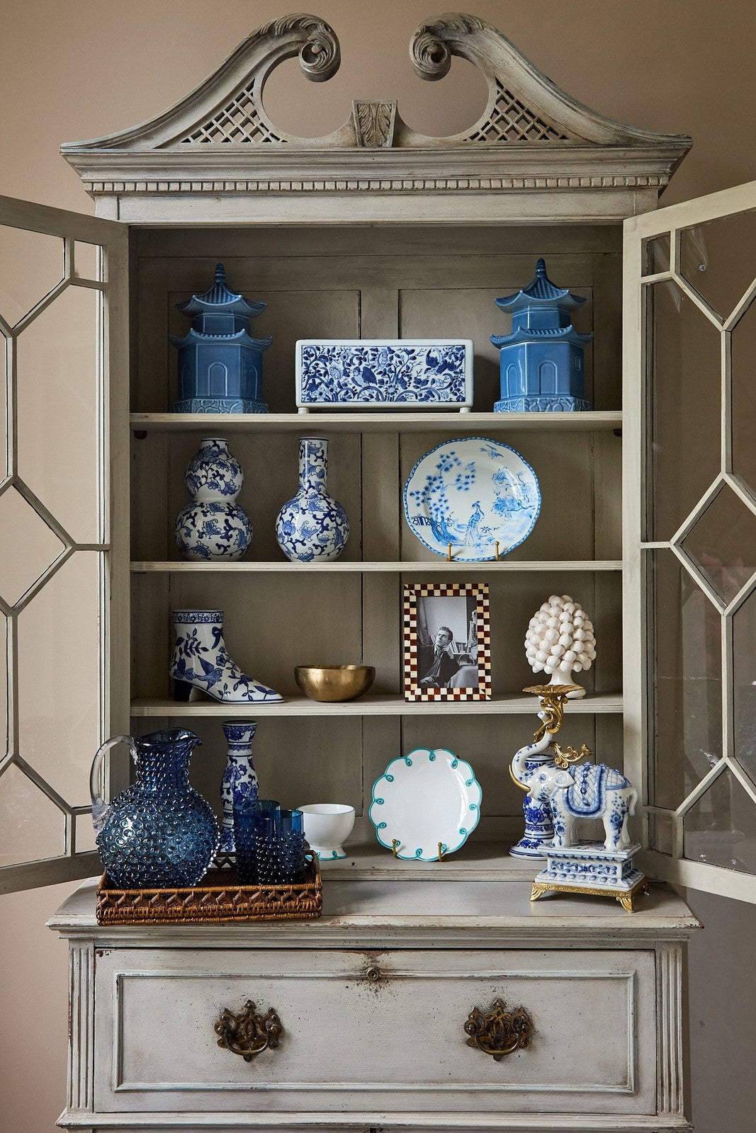 Decorative cabinet with blue and white ceramic items against a beige wall.