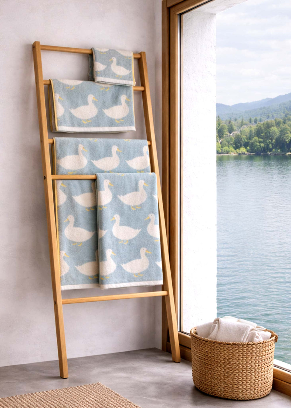 Bamboo ladder with towels featuring duck pattern next to a window with a view of a lake and mountains.