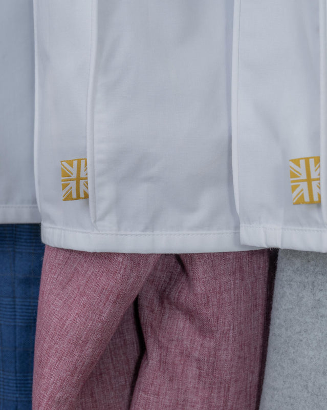 Close-up of a white organic cotton cover with small yellow Union Jack patches near the hem, worn over pink textured trousers.