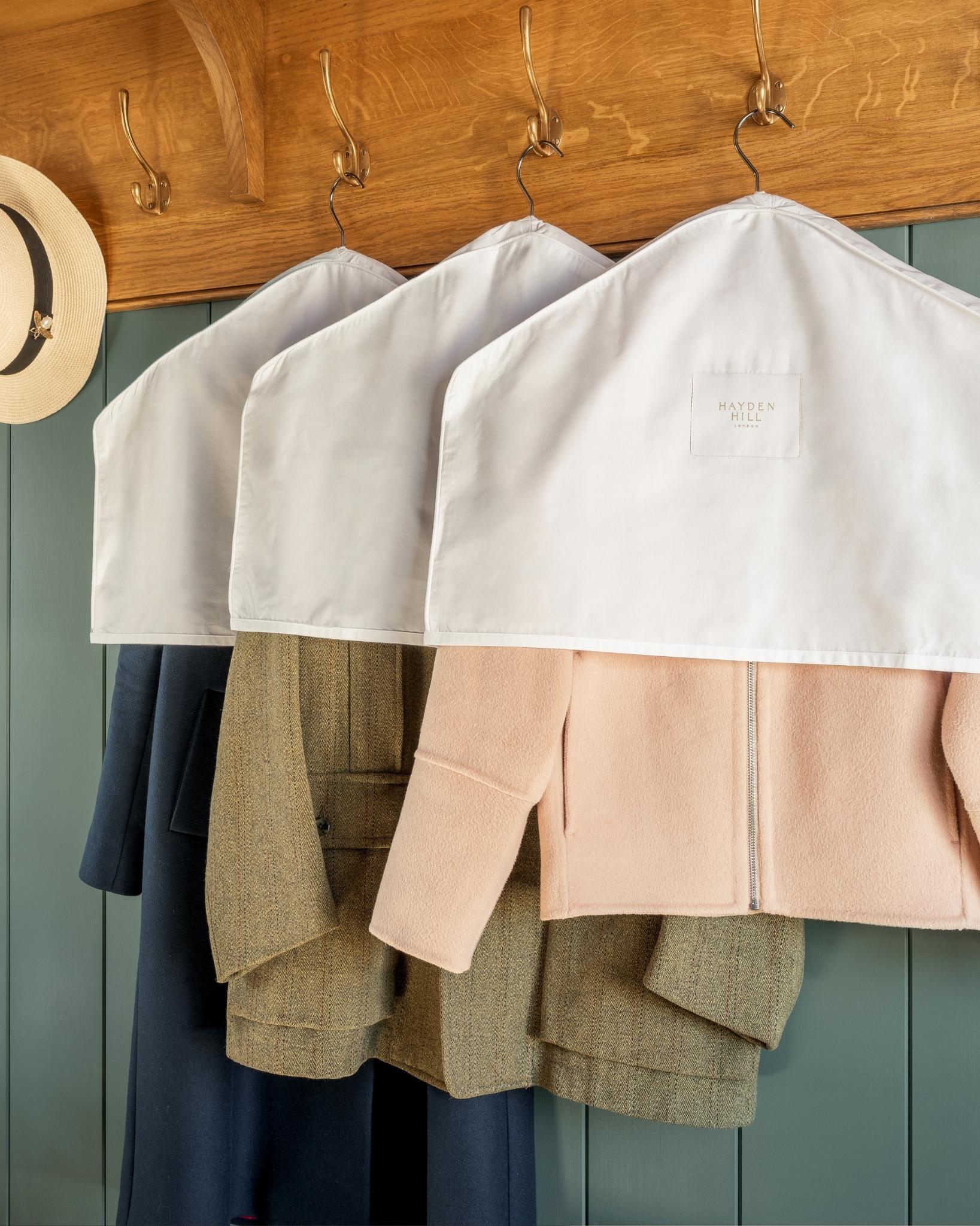 Coats hanging with dust covers on a wooden rack against a green wall