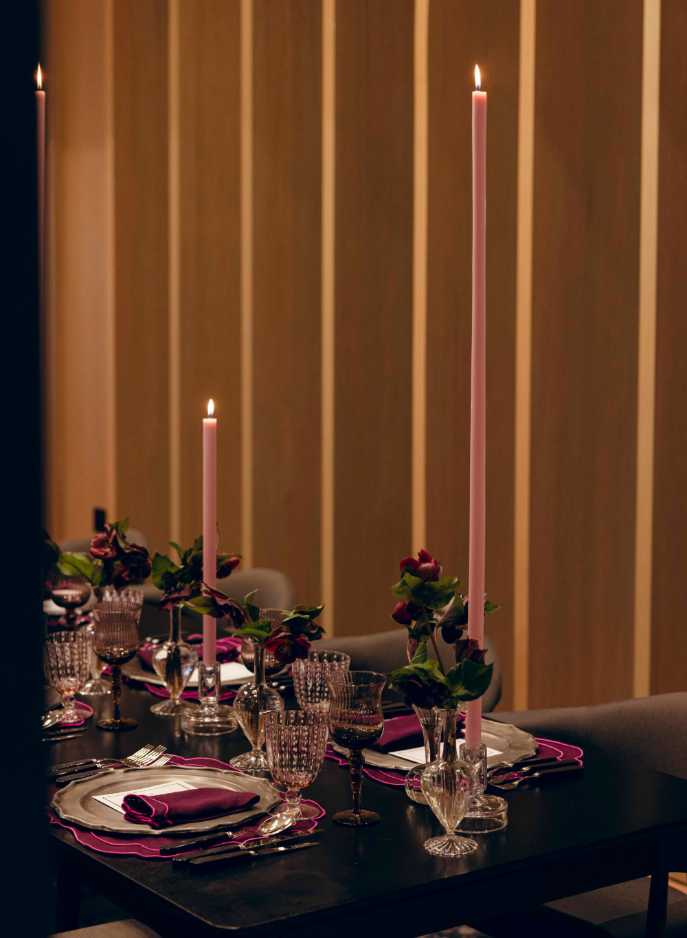 Dining table set with candles and floral arrangements against a striped wall.