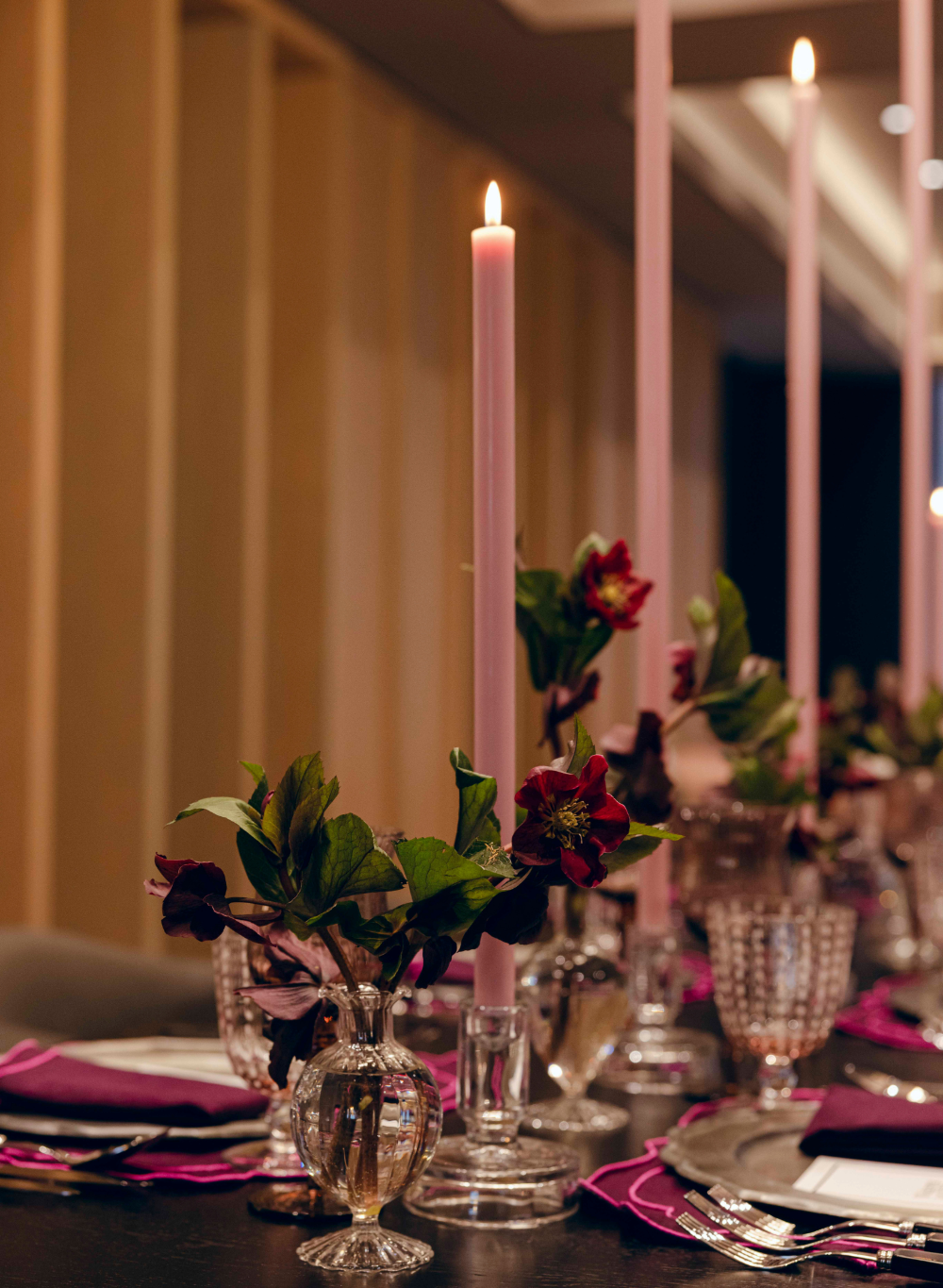 Dining table setting with candles, flowers, and glassware in a dimly lit room.