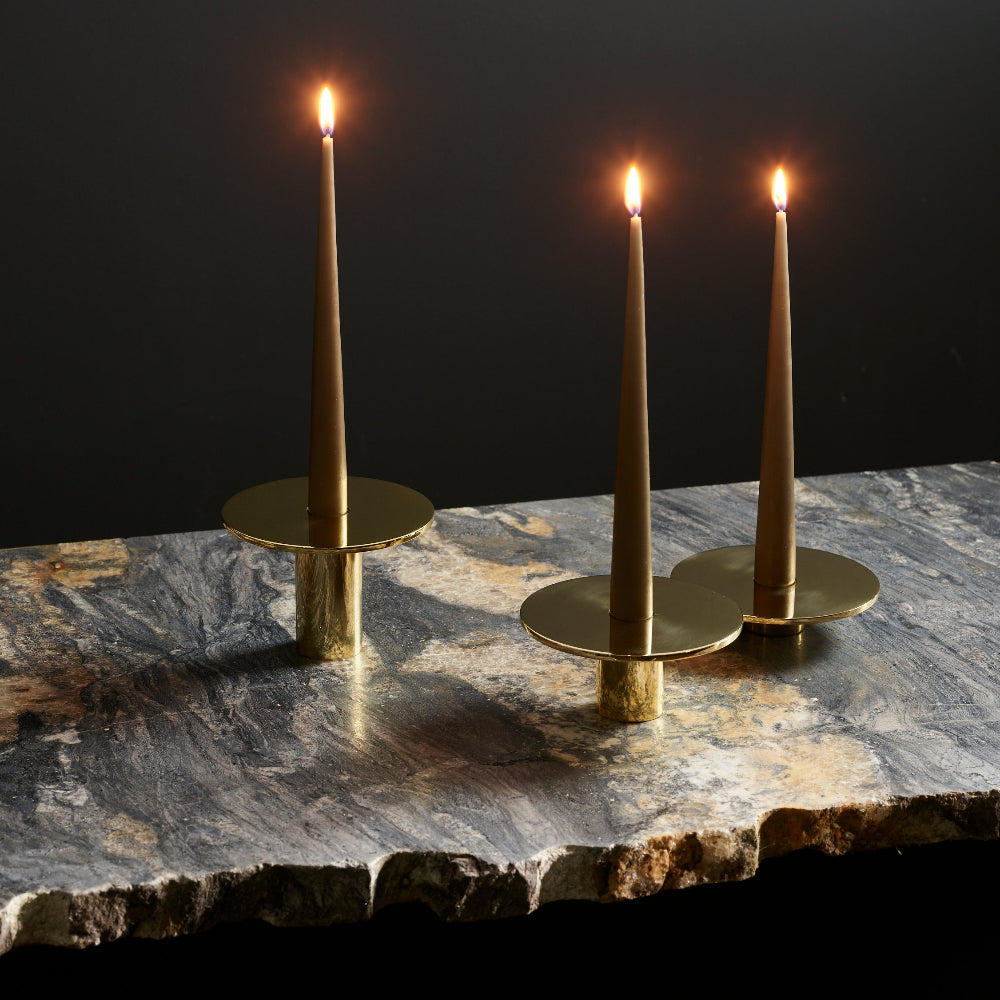 Three brass candlesticks with lit taper candles, arranged on a dark stone slab against a black background.