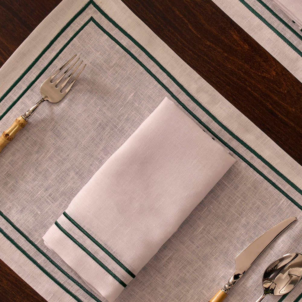 Folded white napkin on a textured placemat with green stripes, accompanied by cutlery.