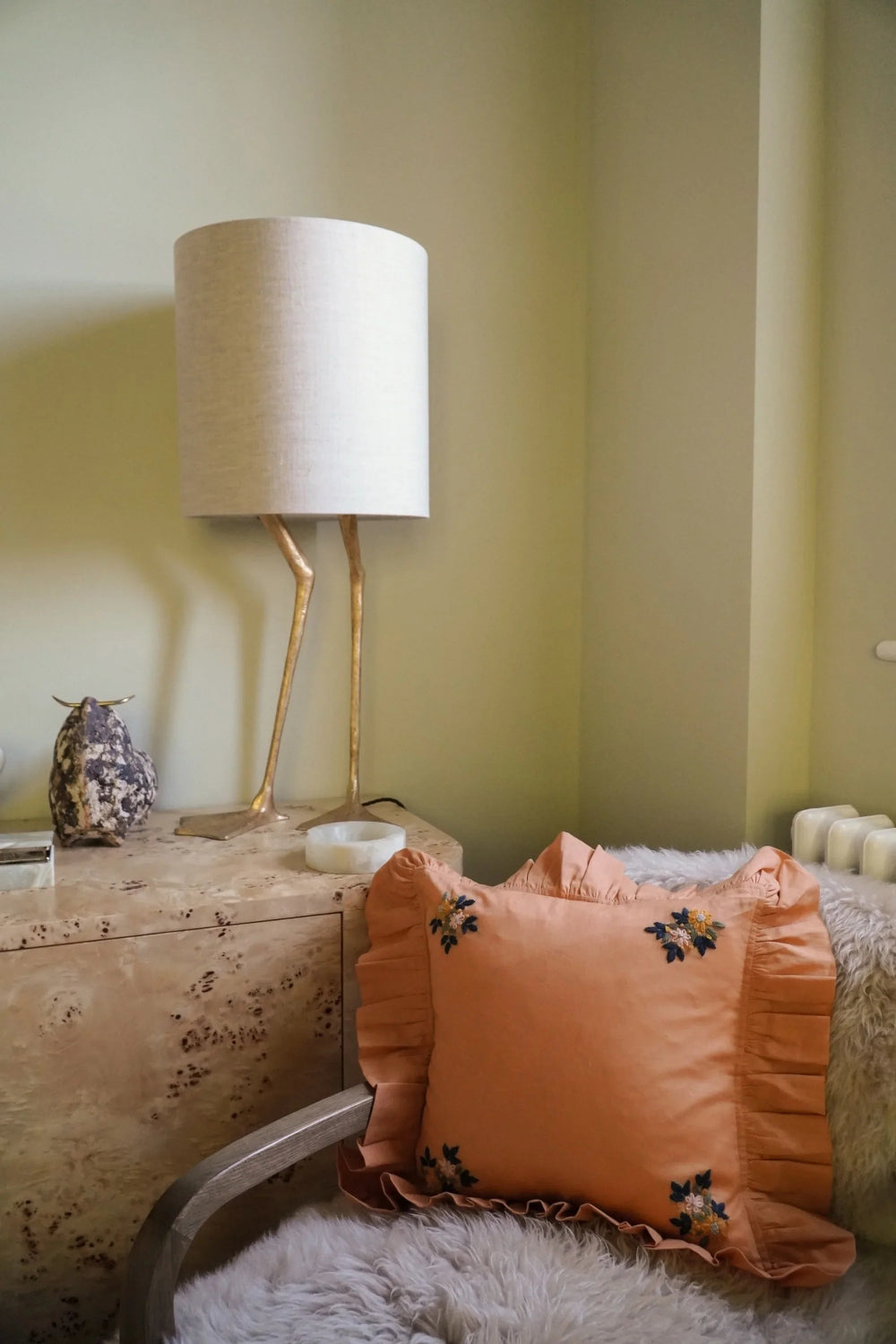 Orange pillow with floral patterns on a textured surface next to a lamp.
