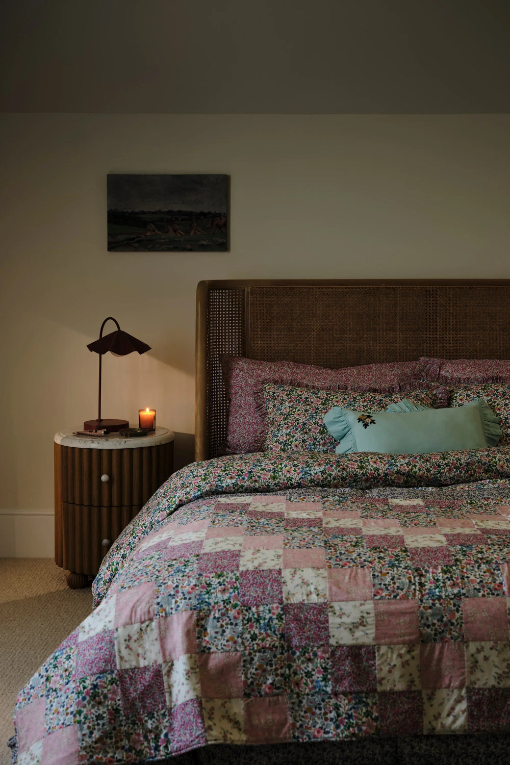 Bedroom with a floral patchwork quilt on a bed, nightstand with lamp, and candle.