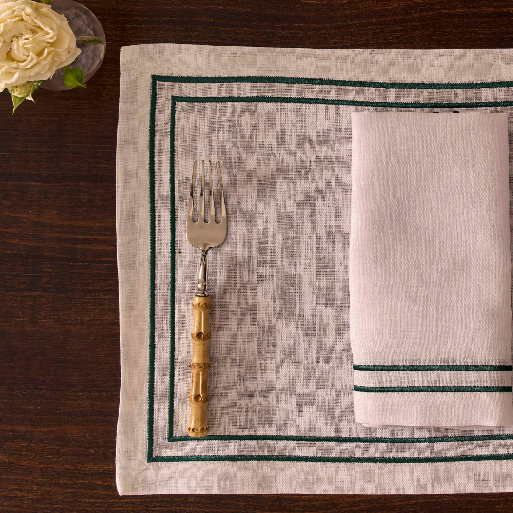 Placemat with green border, fork, and napkin on a wooden table.