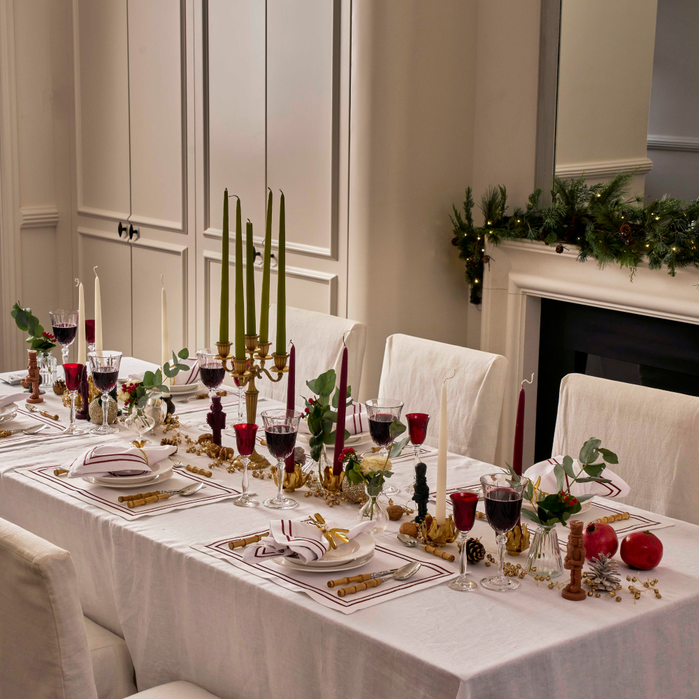 Elegant Christmas dinner table setting with candles, glasses, and place settings in a room with a fireplace.